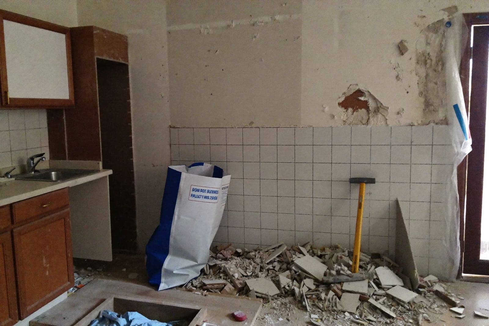 Half uitgebroken oude keuken met puin op de vloer, afgeslagen tegels en gereedschap tegen de muur