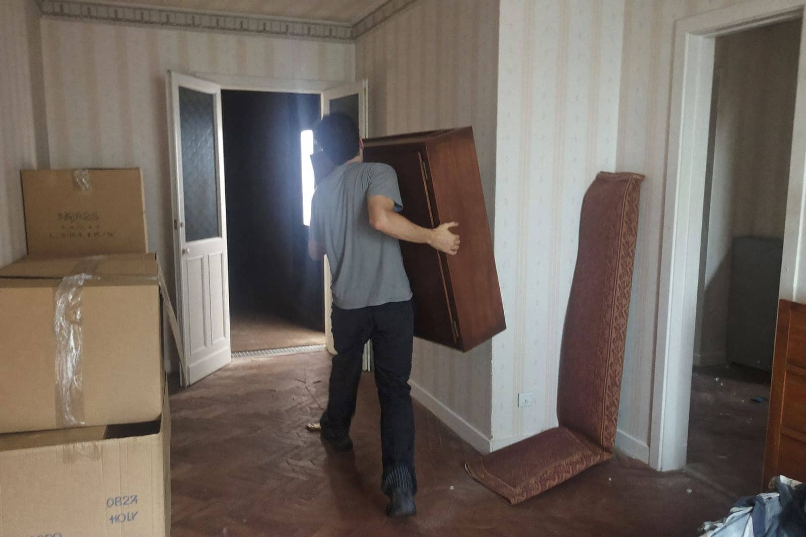 Werkman van Bee Fast draagt een oude houten kast door de gang van een huis dat wordt leeggemaakt
