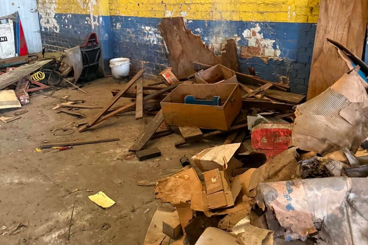 Berg hout, karton en oude rommel opgestapeld tegen de muur van een loods, klaar om afgevoerd te worden