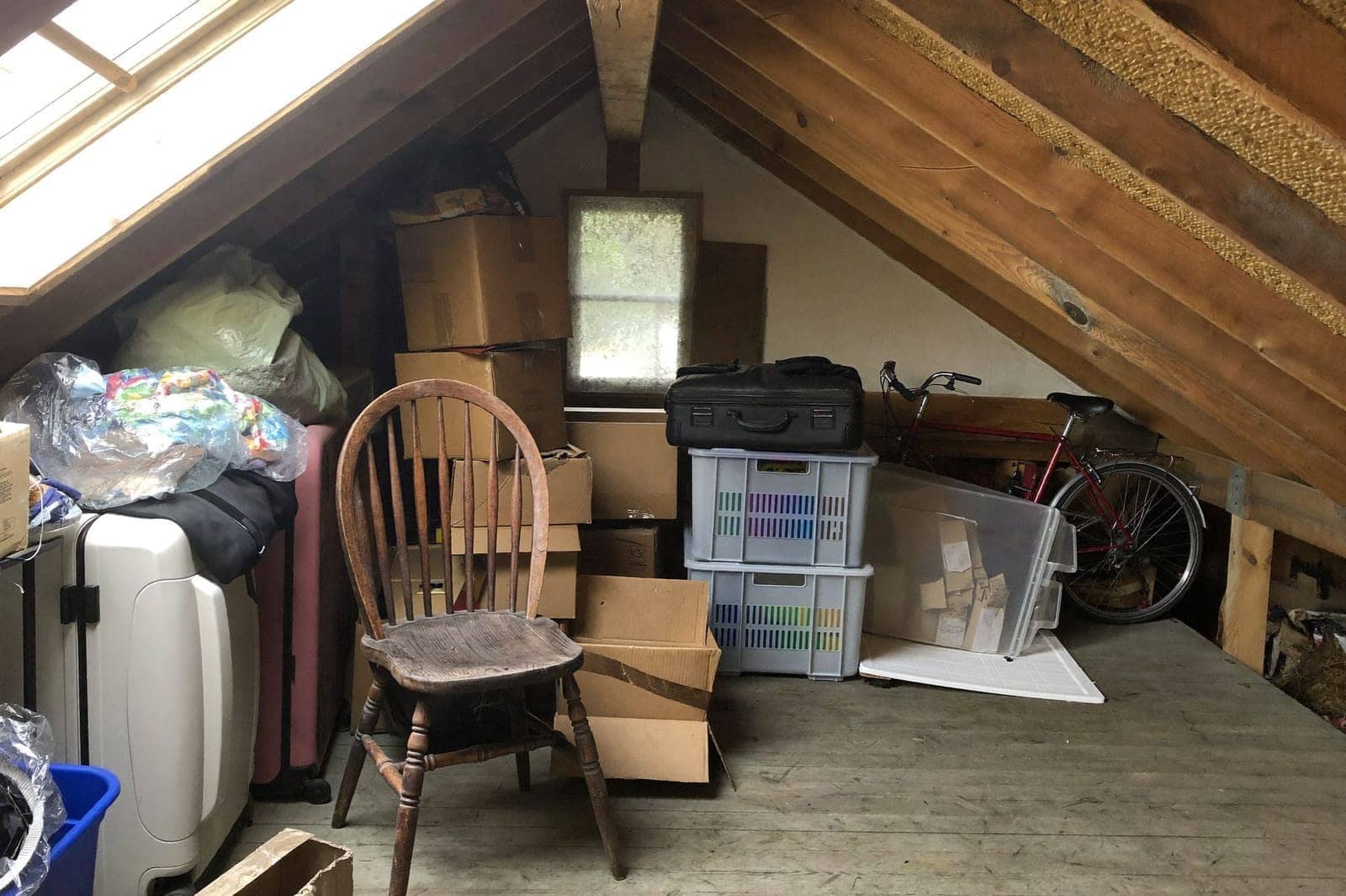 Volle zolder onder houten dakspanten met dozen, koffers en oude spullen die opgeruimd moeten worden